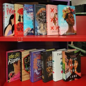 Colorful new young adult books on two shelves of a bright red metal book cart.